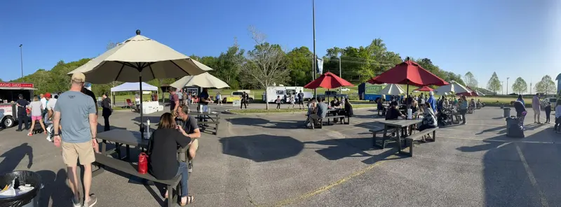 Families at picnic tables under umbrellas during an evening food truck night